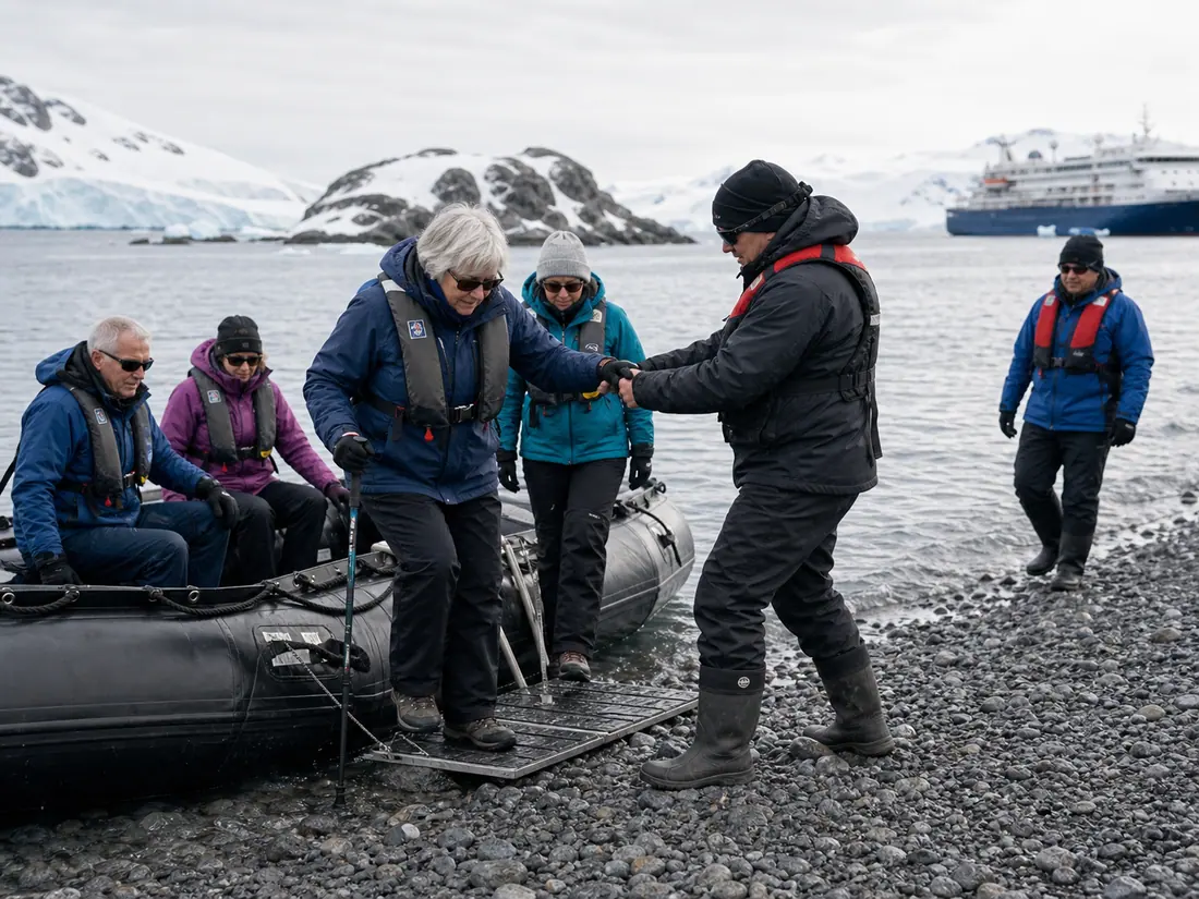 Expedition staff helping an older traveler step ashore from a Zodiac in Antarctica.